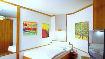 A hotel room with a bed, a TV, and three paintings on the walls.