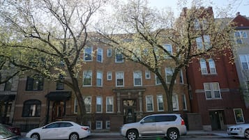 A row of brick townhouses with a central entrance, parked cars, and trees in the foreground.