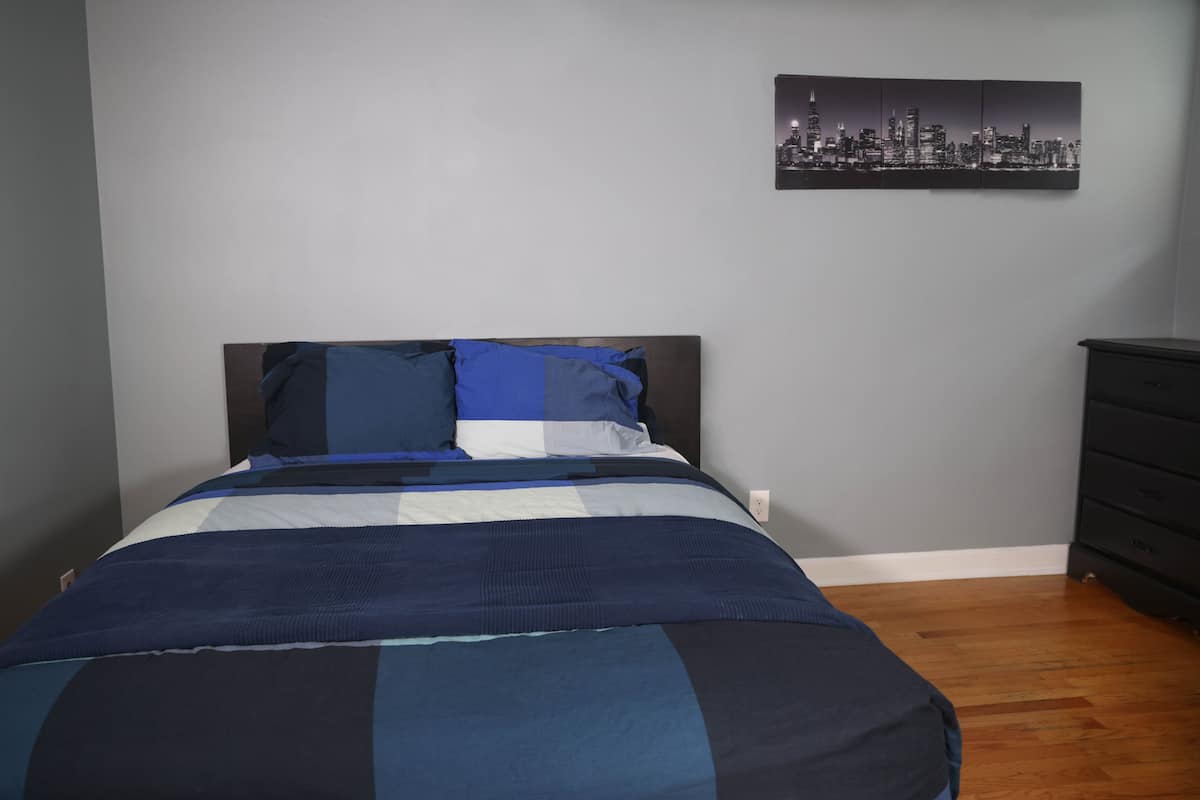 Une chambre à coucher avec un lit, une œuvre d’art représentant un paysage urbain accrochée au mur et une commode.
