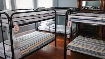 Des lits superposés, chacun étant muni d’une étiquette personnalisée, dans une pièce au plancher en bois et dotée d’un radiateur.