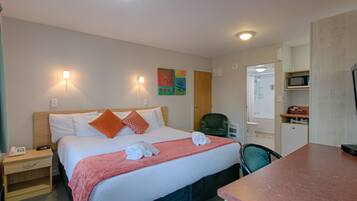 A hotel room with a bed, bedside tables, a desk, a chair, a microwave, and a television.