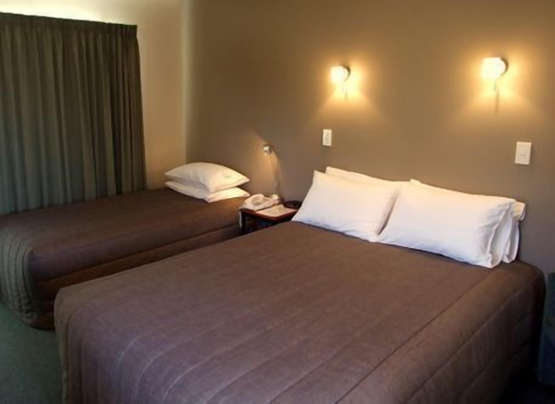 A hotel room with two beds, each with a pillow and a bedside table.
