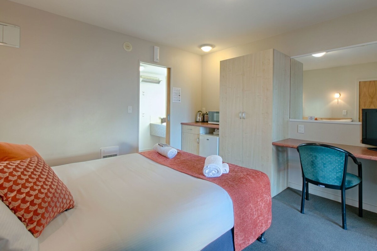 A hotel room with a bed, a desk, a chair, a wardrobe, and a television.