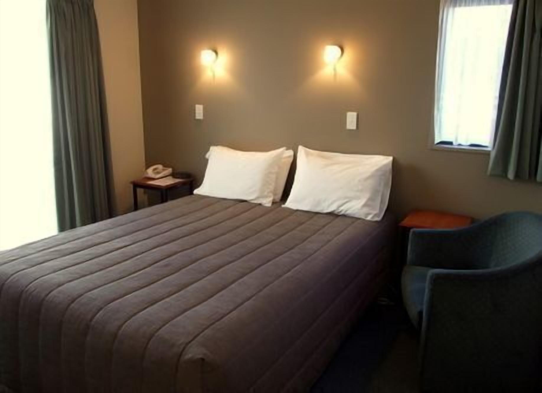 A hotel room with a large bed, two bedside lamps, a chair, and a window.