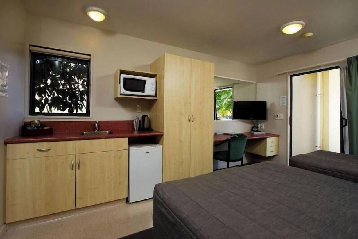 Une chambre d’hôtel compacte comprenant un coin cuisine, un lit, un bureau, une télévision et une fenêtre donnant sur un paysage agréable.