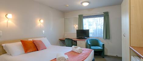 A hotel room with a bed, a desk with a television, a chair, and a wardrobe.