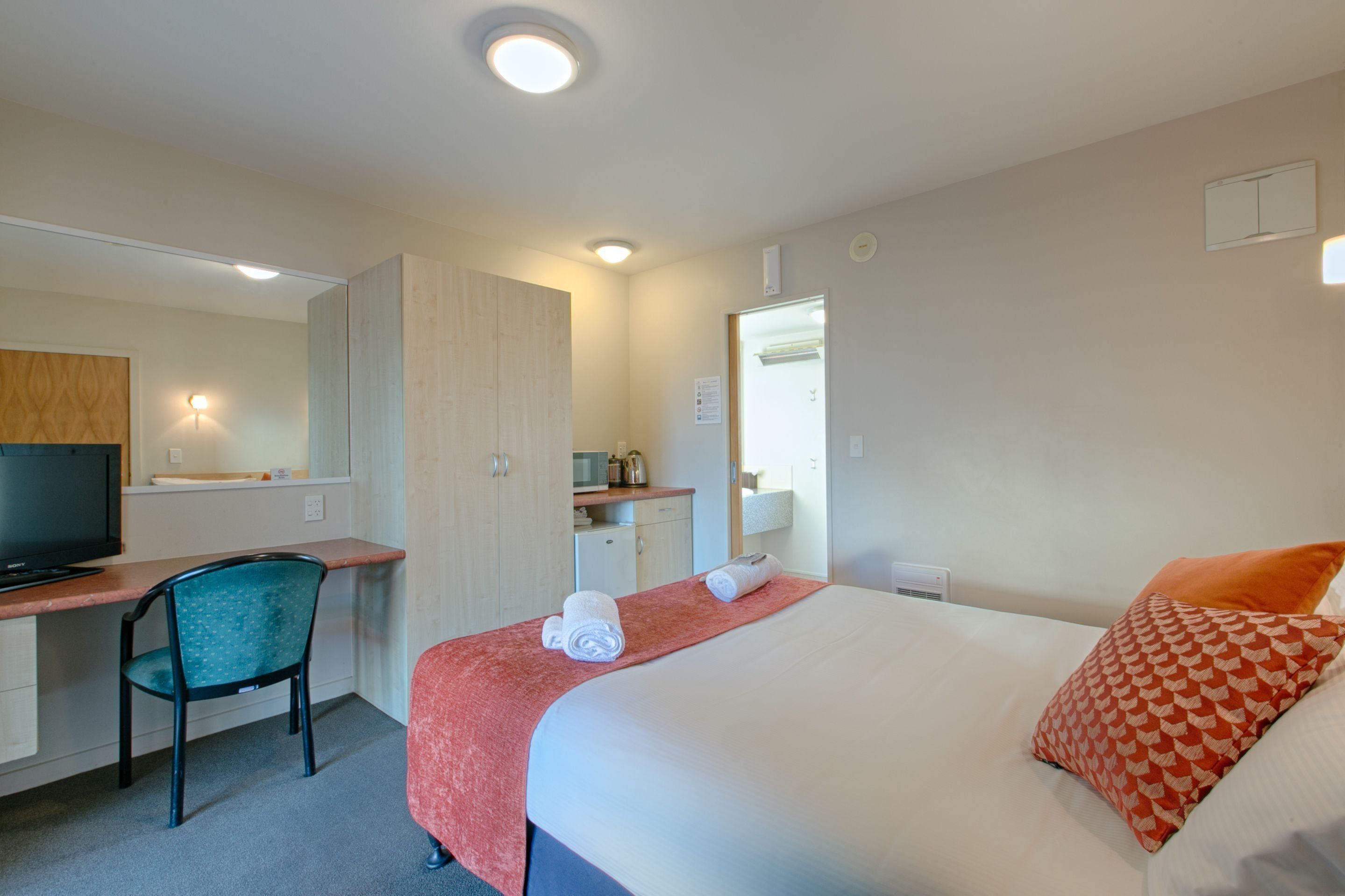 Une chambre d’hôtel équipée d’un lit, d’un bureau, d’une chaise, d’une télévision et d’une kitchenette.