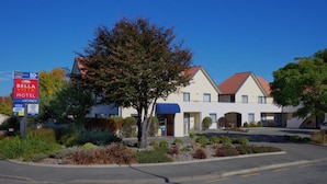 Een motel met een blauw luifel, een boom ervoor en een heldere blauwe lucht.