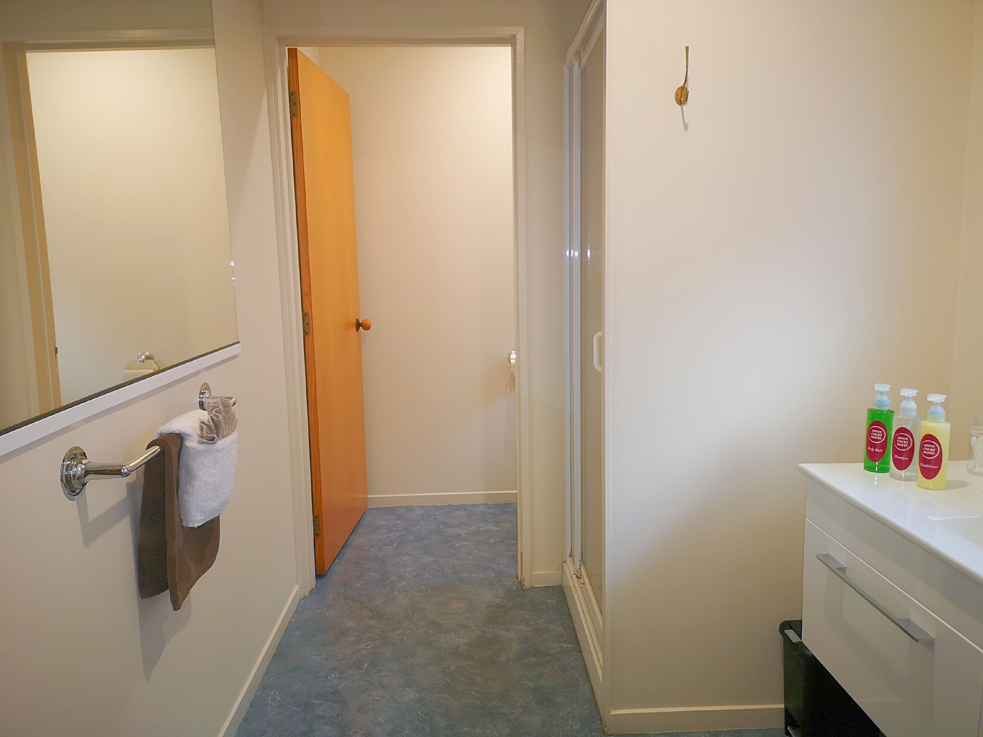 A bathroom with a white sink, a mirror, and a towel rack. There are three bottles of shampoo on the sink.