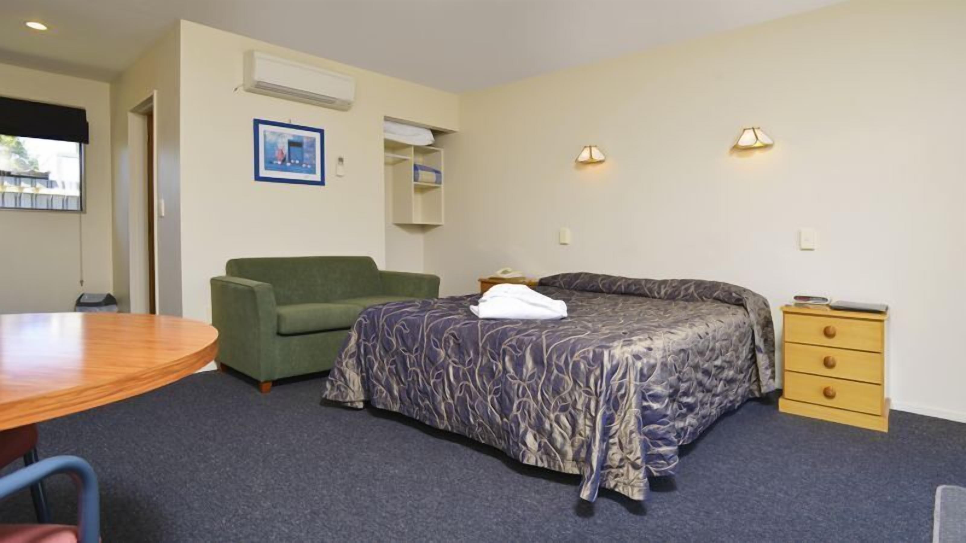 Une chambre d’hôtel avec un lit, un canapé vert, une table en bois, une petite commode et un tableau au mur.