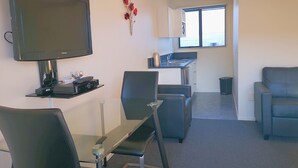 A modern living room with a flat-screen TV, a dining table with chairs, a sofa, and a kitchen area with a window. - Aston Court Motel Blenheim (Blenheim)