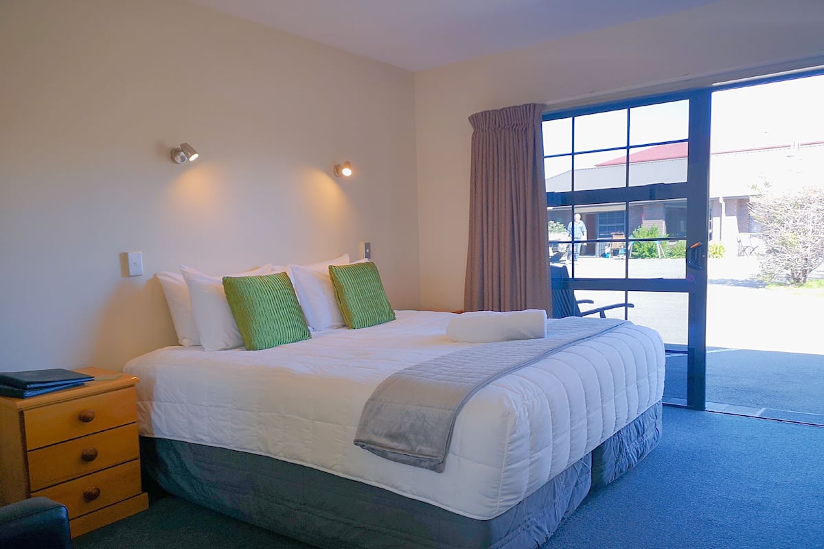 A hotel room with a large bed, a nightstand, a desk, and a window with a view of the outside.