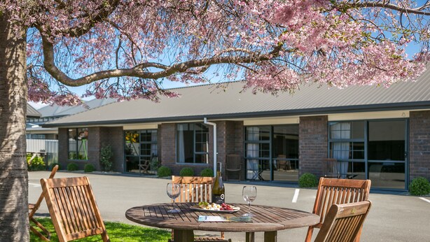 An outdoor dining area with a round table and wooden chairs, a bottle of wine, and a plate of food. - Aston Court Motel Blenheim (Blenheim)