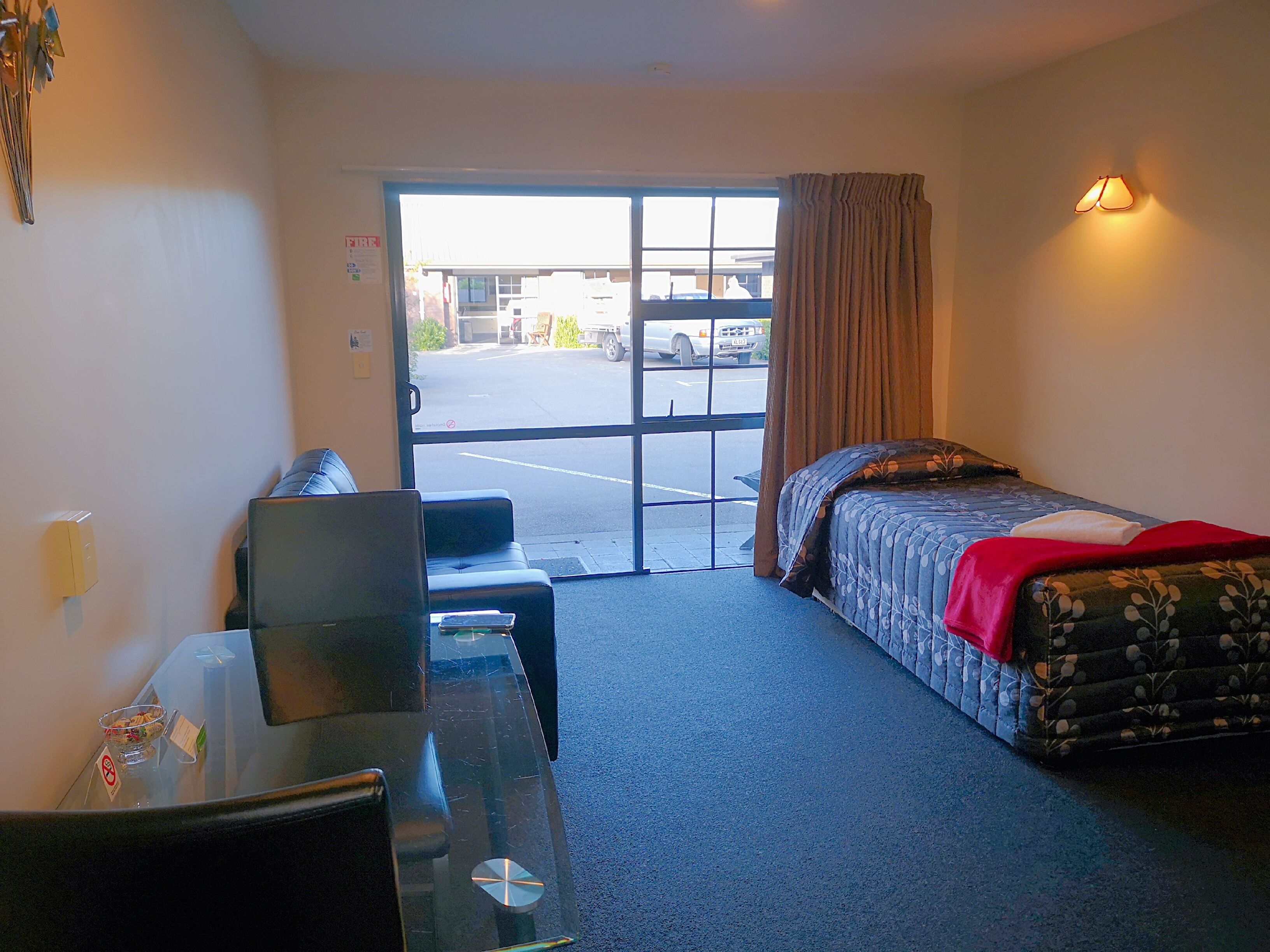 Una habitación de hotel con cama, escritorio, silla y ventana con cortinas.