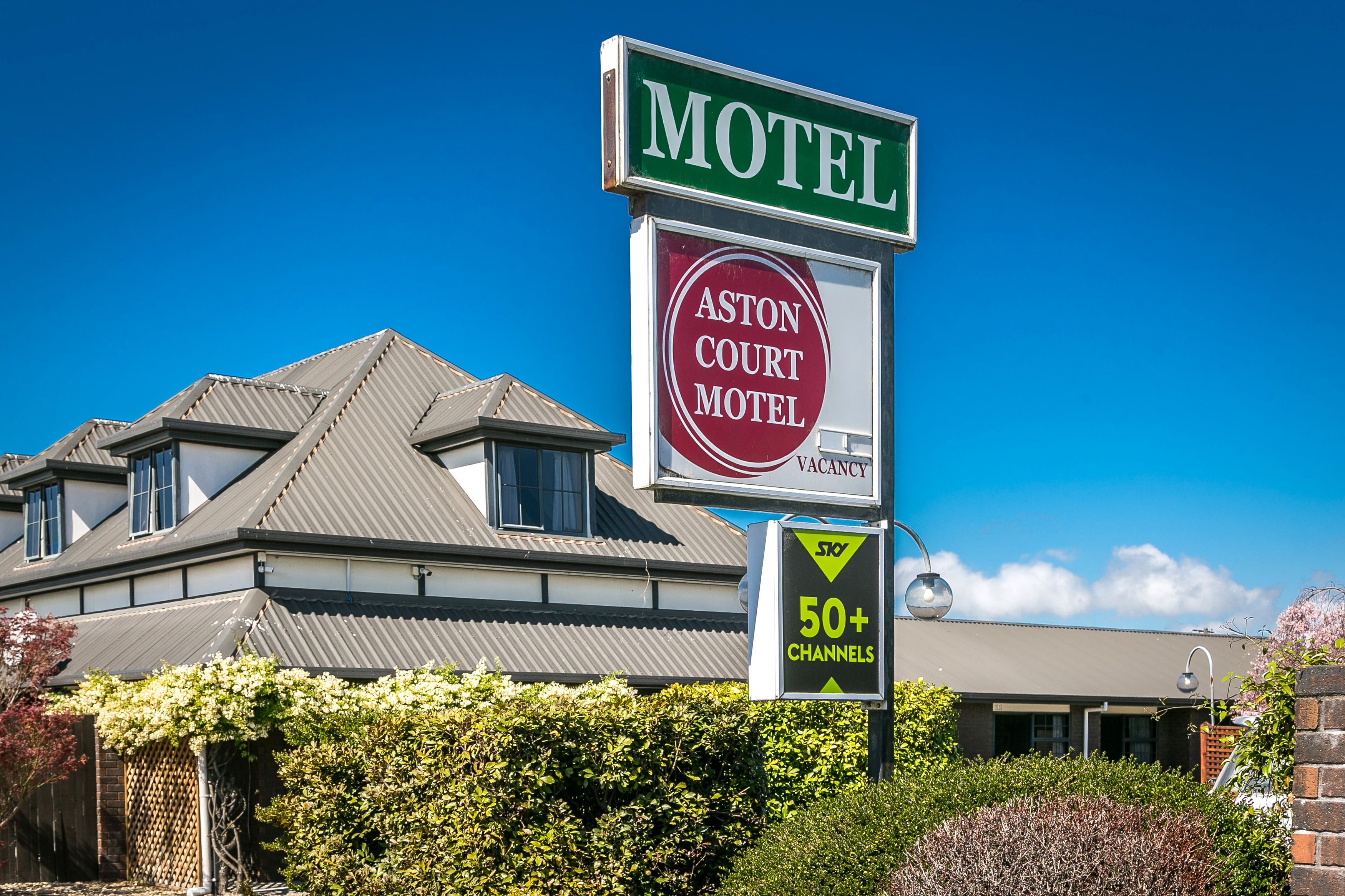 A motel sign with a vacancy notice, a 50+ channels sign, and a building with a grey roof and windows.