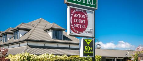 A motel sign with a vacancy notice, a 50+ channels sign, and a building with a grey roof and windows.