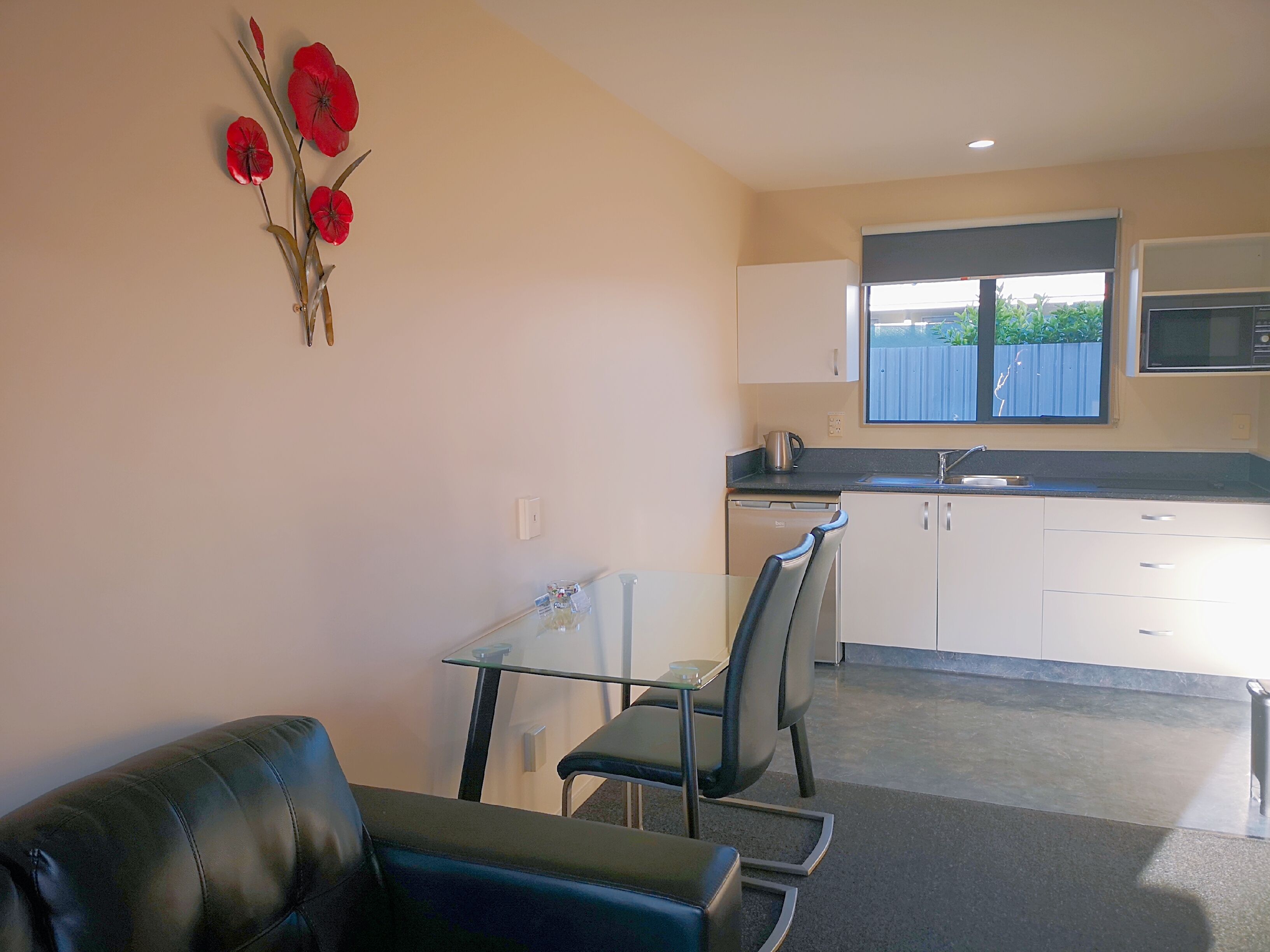 A compact living space with a kitchenette, a dining area with a glass table and chairs, and a black leather couch.