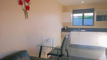 A compact living space with a kitchenette, a dining area with a glass table and chairs, and a black leather couch.