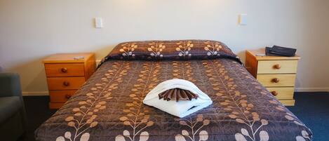 A neatly made bed with a patterned bedspread, a folded towel, and a laptop on a wooden nightstand.
