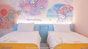 Hotelkamer met twee bedden, een muurschildering van Hello Kitty en een strandscène.