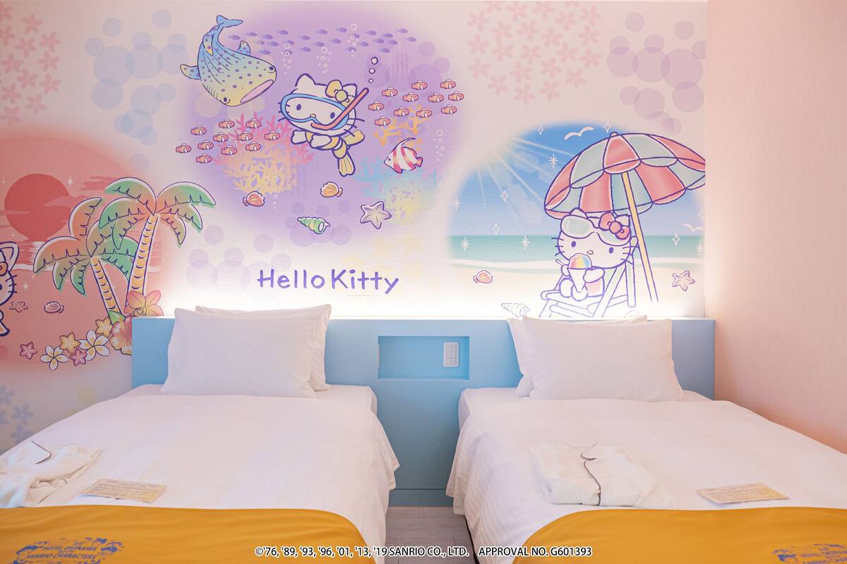 A hotel room with two beds, a mural of Hello Kitty, and a beach scene.