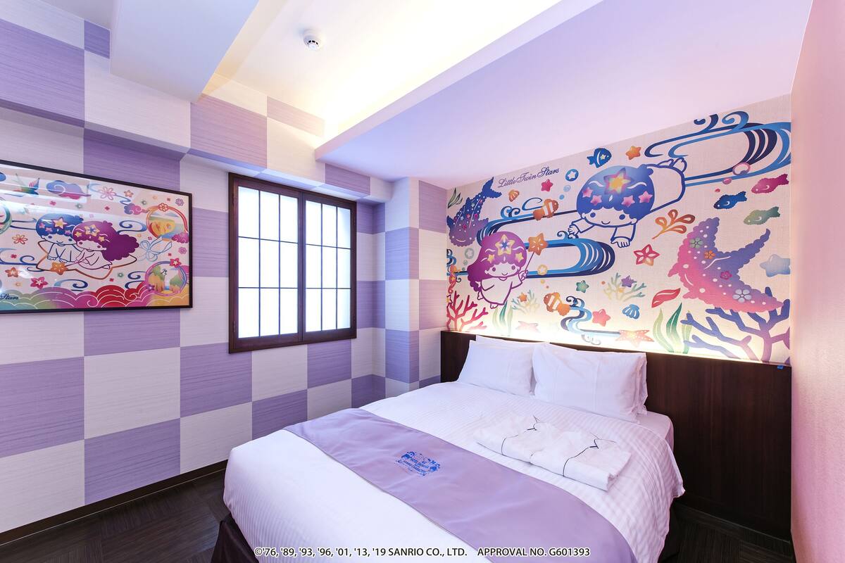 A hotel room with a checkered wall pattern, a large bed with white linens, and two colorful wall murals.