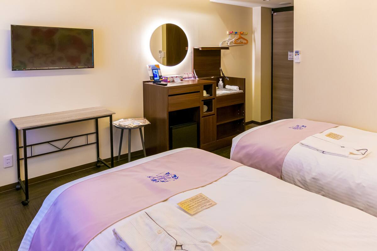 A hotel room with two beds, a desk, a mirror, and a wardrobe.
