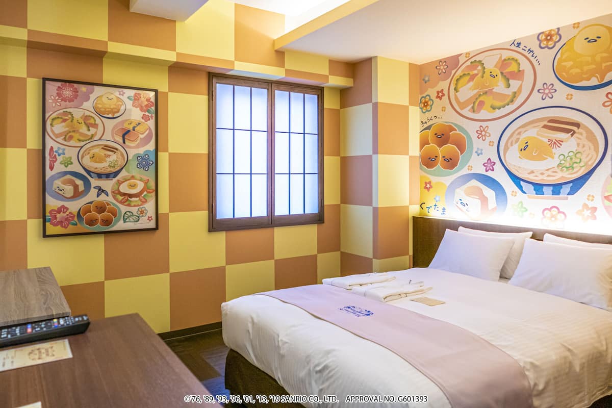 A hotel room with a checkered wall pattern, a bed with white linens, a bedside table with a remote control, and a window with a view.