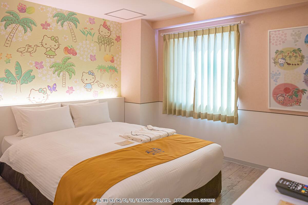 A hotel room with a neatly made bed, a window with curtains, and a wall with a Hello Kitty mural.