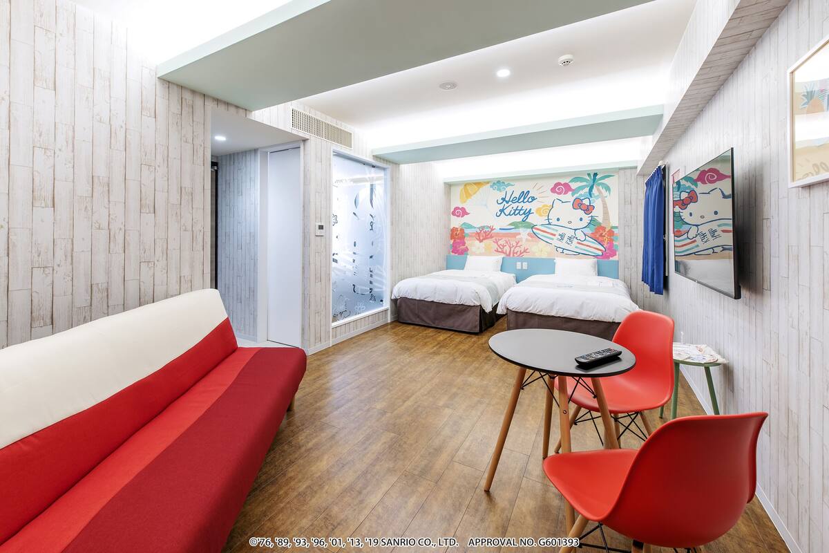 A hotel room with a red sofa, two beds, a small table, and red chairs.