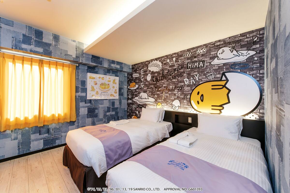 A hotel room with two beds, a brick-patterned wall, and a mural with cartoon characters.