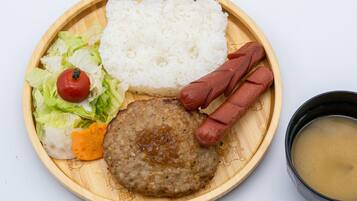 Un plato con arroz blanco, una hamburguesa, salchichas, un tomate, lechuga y un tazón de sopa.