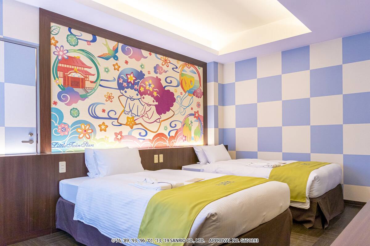 A hotel room with two beds, a colorful mural on the wall, and a checkered blue and white wall pattern.