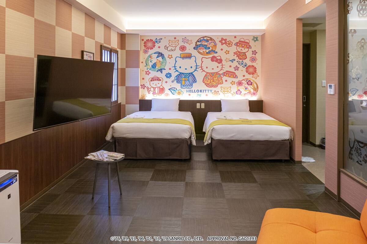 A hotel room with two beds, a flat-screen TV, and a wall decorated with Hello Kitty characters.