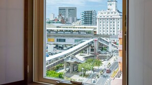 Een stadsgezicht door een raam, met moderne gebouwen, een voetgangersbrug en een heldere lucht.