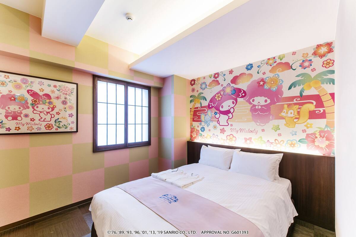 A hotel room with a bed, a window, and colorful wall art.