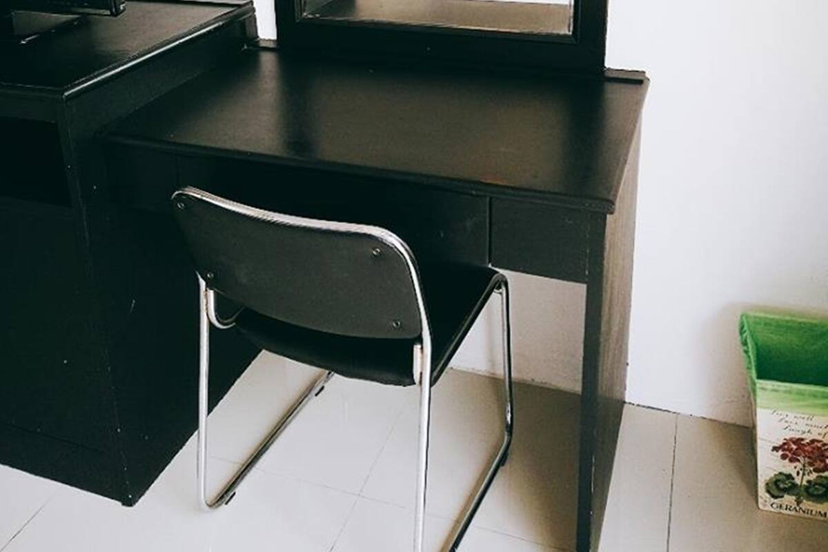 A compact hotel room with a black desk, a chair, a bed with white bedding, and a large mirror.