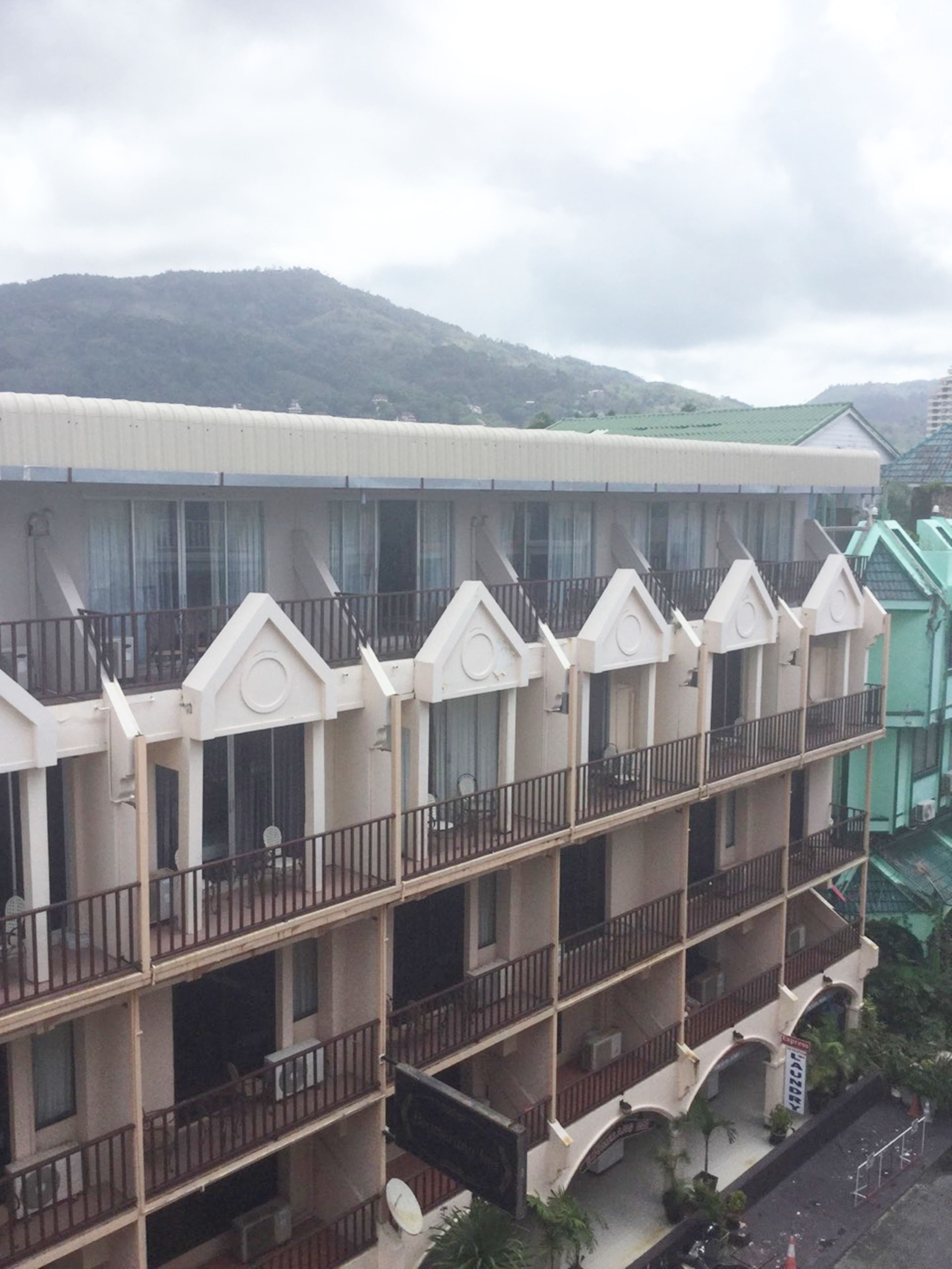 Um hotel com vários andares, varandas, telhado plano e vista para uma montanha.