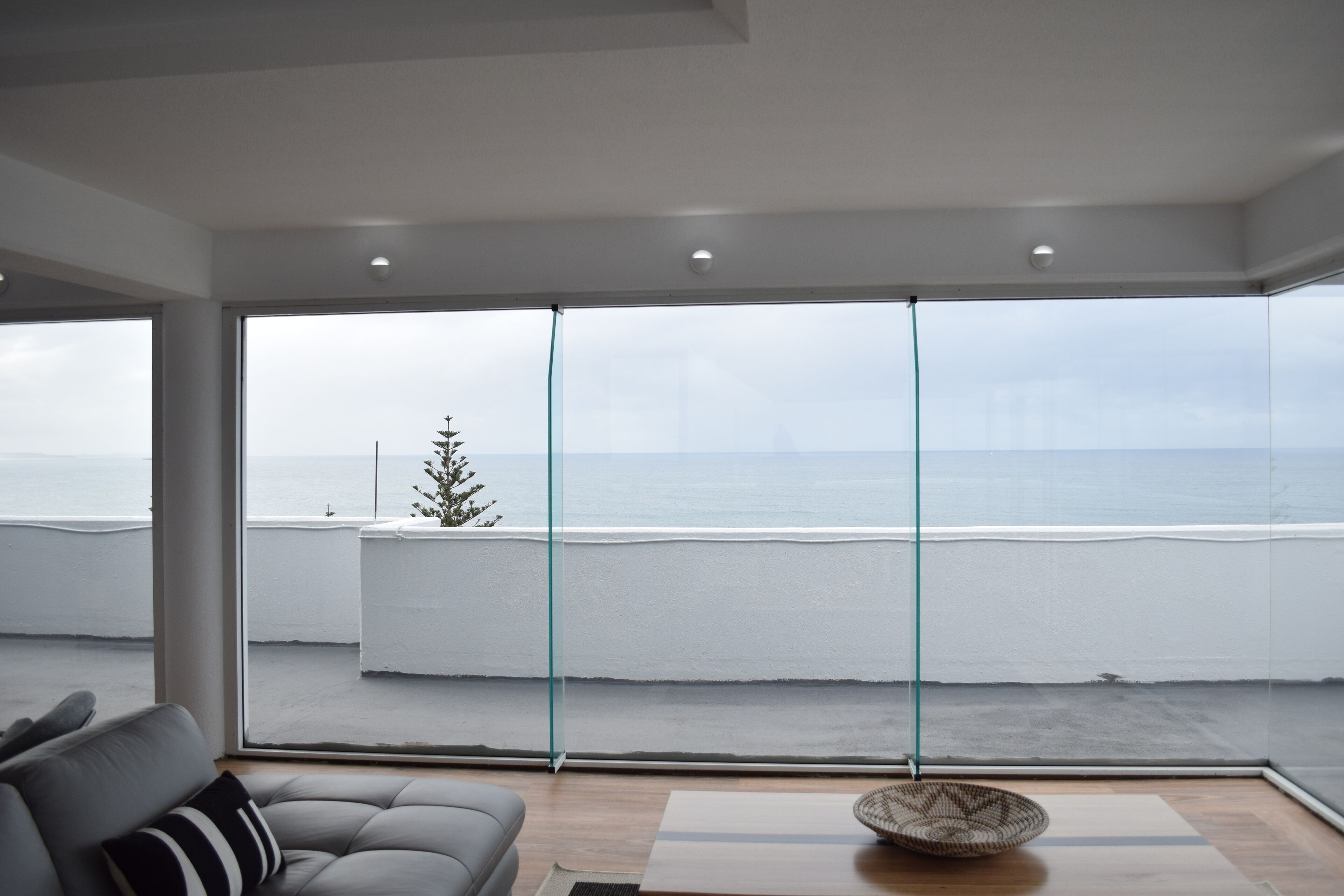 Un salon moderne doté d’une grande baie vitrée donnant sur un balcon avec vue sur la mer.