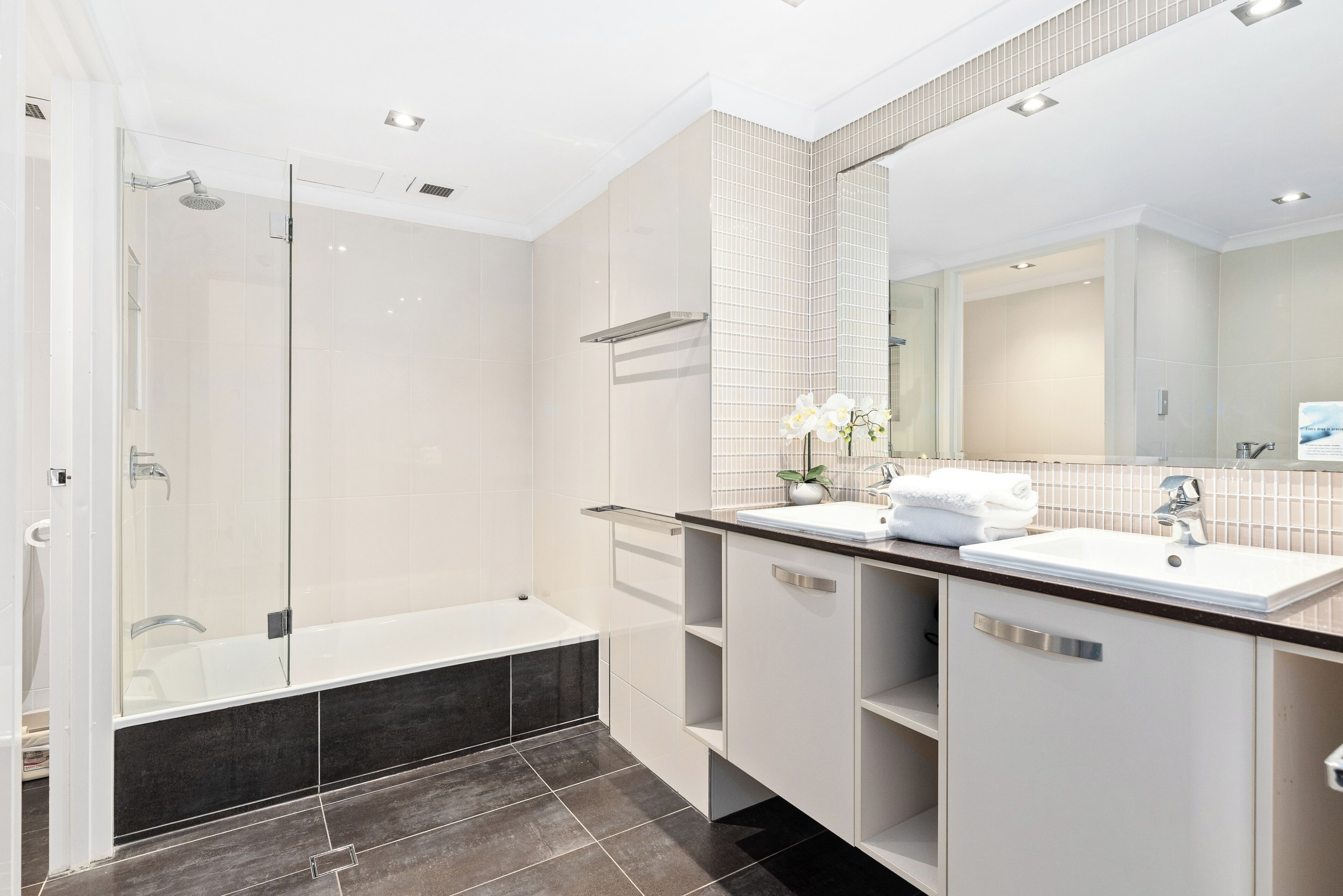 Un baño moderno con ducha de vidrio, bañera, tocador con lavabo y un espejo grande.