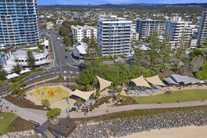 Un quartier urbain moderne, avec de hauts immeubles, un parc central doté d’espaces de repos ombragés et une vue sur la côte.