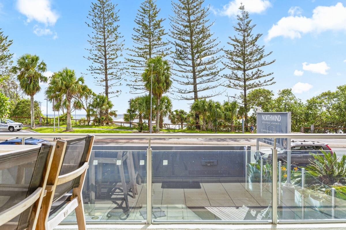 A modern building with a glass facade, surrounded by palm trees and a clear sky.