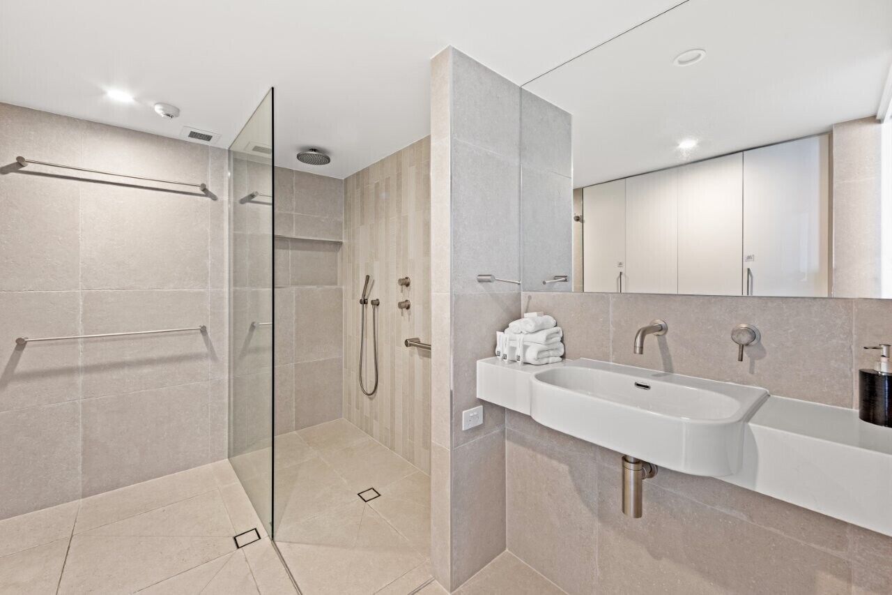 A modern bathroom with a glass-enclosed shower, a white sink, and a large mirror.