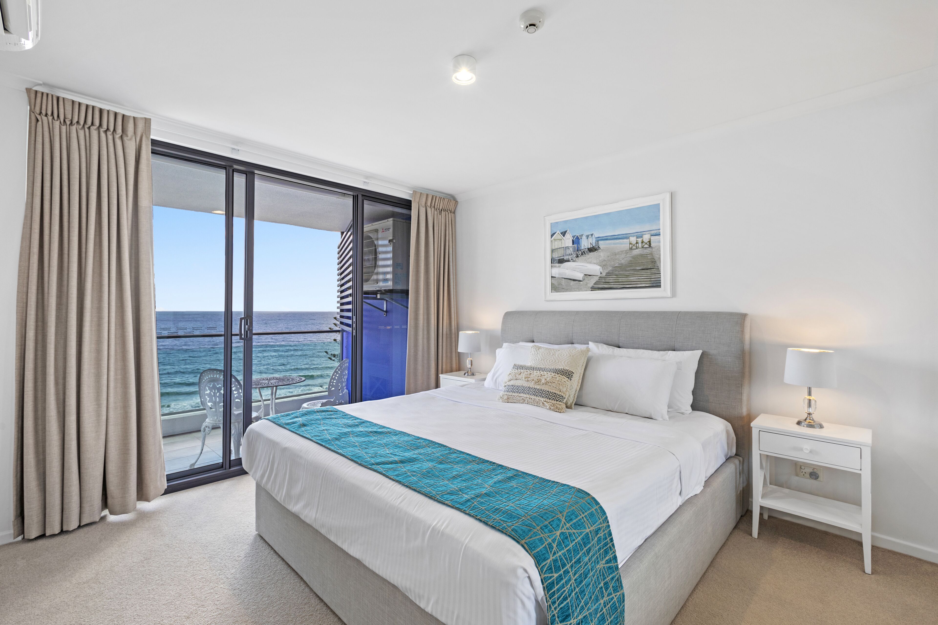 Habitación de hotel con una cama grande, vista al océano y un balcón con cortinas.