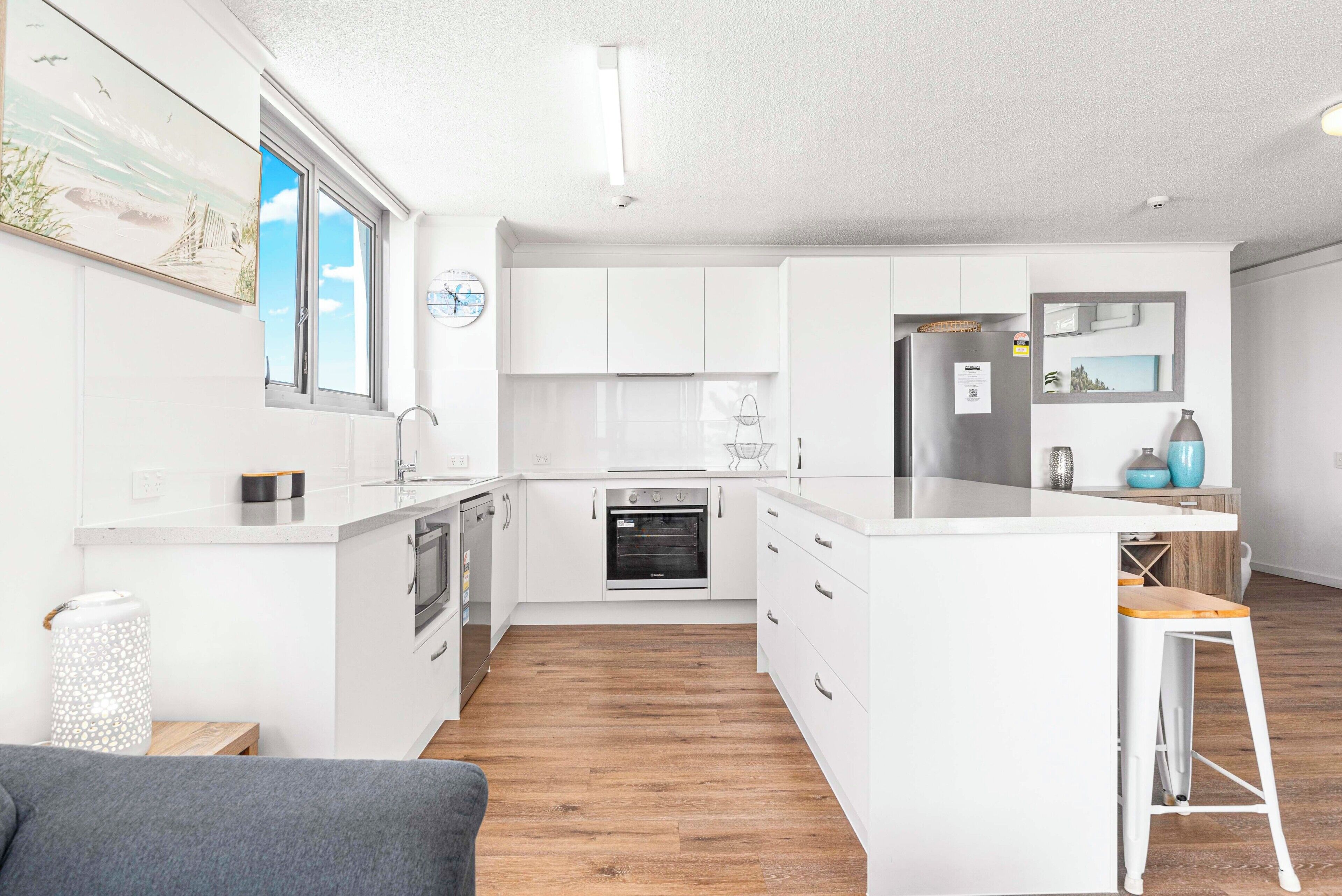 A modern kitchen with white cabinetry, a built-in oven, and a wooden floor.