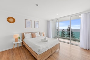 Une chambre avec un grand lit, une petite table de chevet, une caméra fixée au mur et une vue sur la mer, visible à travers une porte-fenêtre coulissante.