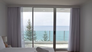 A bedroom with a large bed, a view of the sea through a sliding glass door, and a potted plant. - Northwind Holiday Apartments Mooloolaba (Mooloolaba)