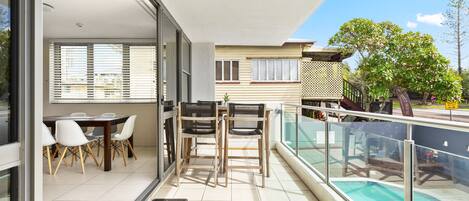 A modern apartment with a balcony, a dining area with chairs and a table, and a view of a swimming pool.