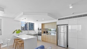 A modern kitchen with white cabinetry, a central island, and bar stools. - Northwind Holiday Apartments Mooloolaba (Mooloolaba)