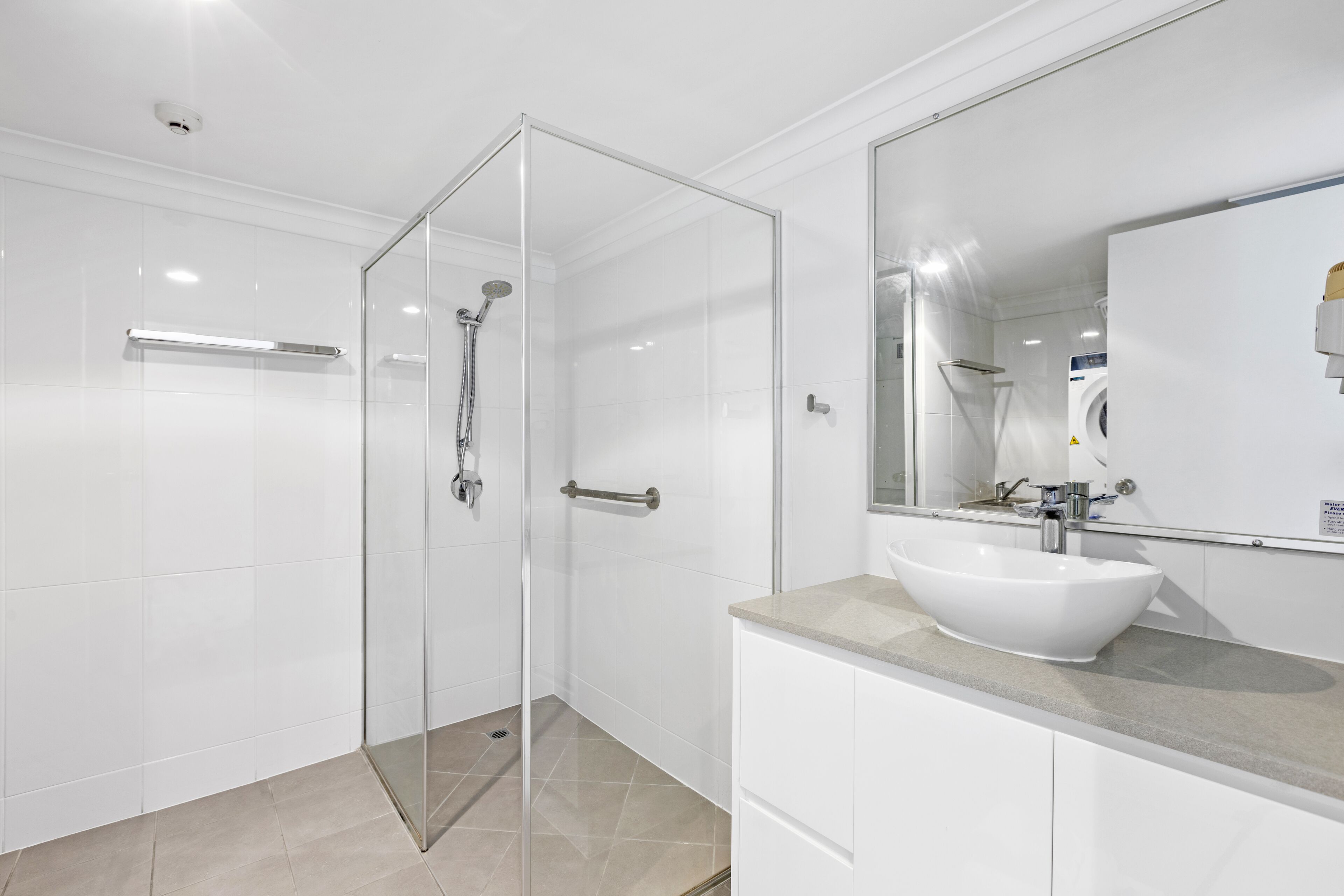A modern bathroom with a glass shower enclosure, a white sink, and a large mirror.